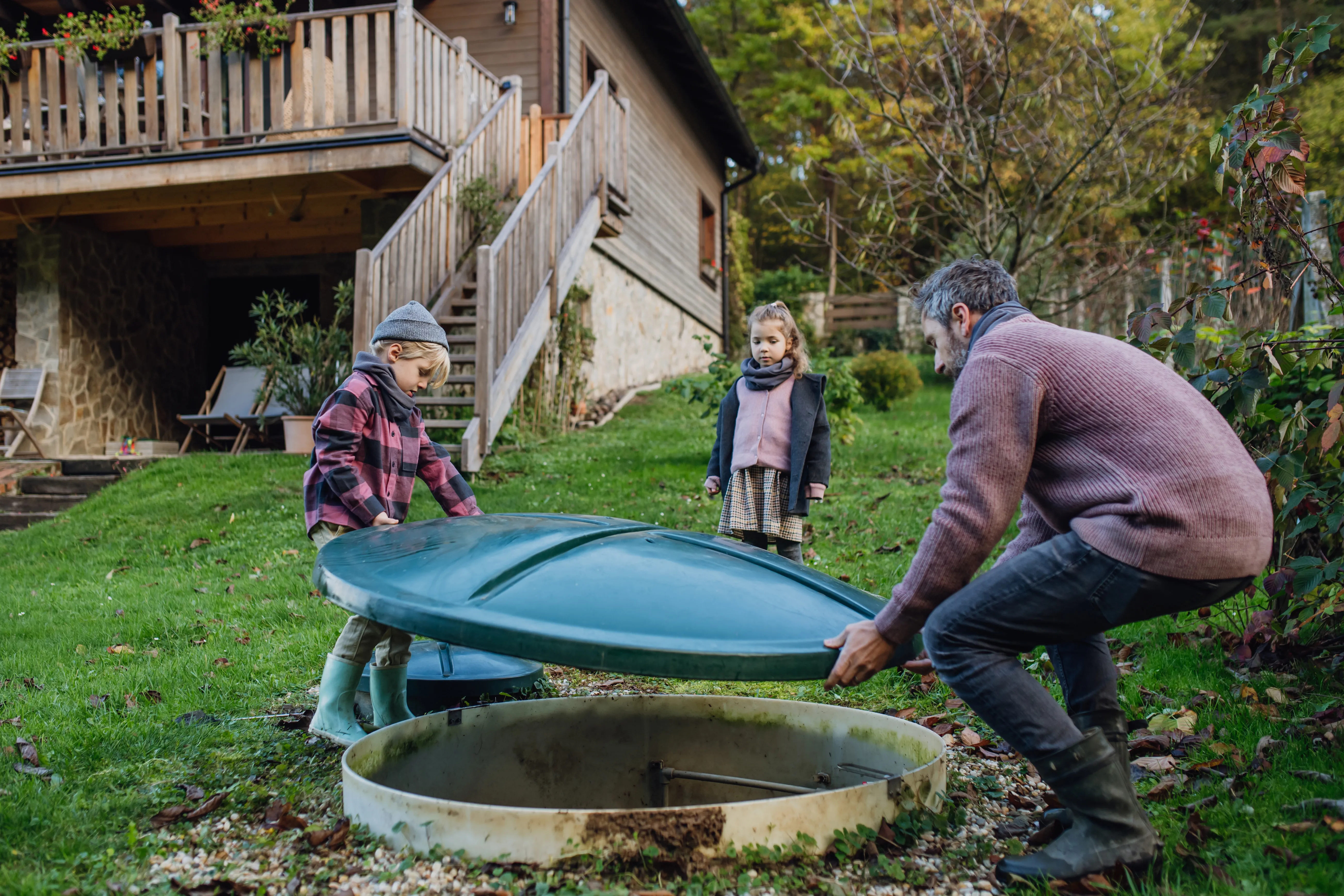 A family opening the access cover of a septic tank in their garden